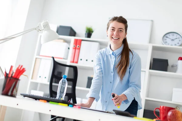 En ung flicka på kontoret stående nära bordet och håller en gul markering i handen. — Stockfoto