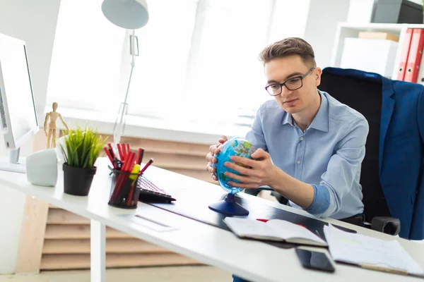 Молодой человек сидит в офисе за компьютерным столом и держит глобус в руках.. — стоковое фото