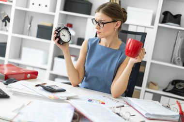 Genç bir kız onun ofisinde bir çalar saat ve kırmızı bir fincan tutan bir masada oturuyor.