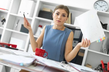 Genç bir kız ofiste bir masada oturur ve onun elinde tutan bir belge ve bir kalem.