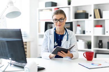 Beyaz bir elbise içinde genç bir kız ofiste bir masada oturur ve bir kalem ve defter elinde tutar. Bir stetoskop boynunda asılı.