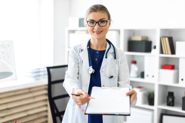 Bir genç kız Beyaz paltolu bir tablo ofisinde yakınındaki duran ve bir tablet ve kalem tutan. Bir stetoskop boynunda asılı.