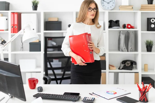 Une jeune fille se tient près d'une table dans le bureau et tient un dossier avec des documents . — Photo