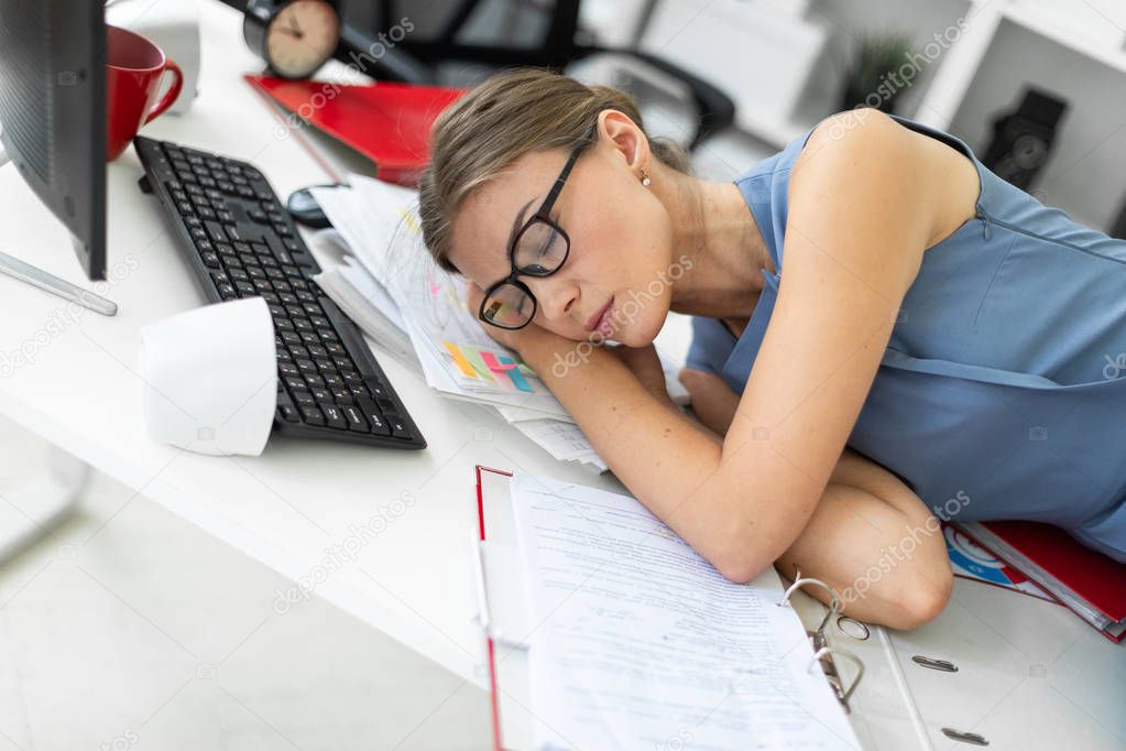 Young girl lies with closed eyes on documents on desk in office.