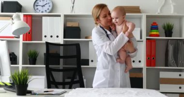 kollarında gülümseyen bebek tutan ve kameraya bakarak çocuk doktoru