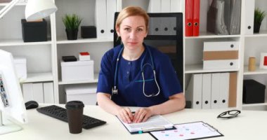 çene ve kameraya bakarak el ile işyerinde oturan doktor