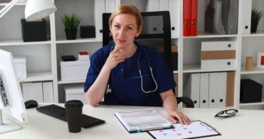 çene ve kameraya bakarak el ile işyerinde oturan doktor