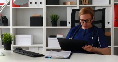 İşyerinde oturan ve belgeleri işaretleme mavi önlük doktor