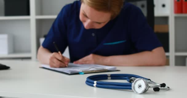 Female Doctor Filling Papers Table Blue Stethoscope Foreground — Stock Video