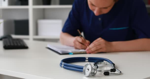 Female Doctor Filling Papers Table Blue Stethoscope Foreground — Stock Video