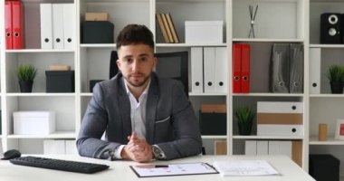 Genç yetişkin iş adamı modern ofiste kameraya bakıyor.