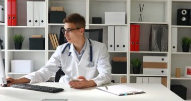 Telefon elinde tutarak ve bilgisayar başında çalışan genç doktor