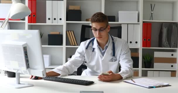 Unga Läkare Håller Telefonen Handen Och Arbetar Dator — Stockvideo