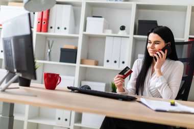 Genç bir kız bir masada oturuyor, bir banka kartı elinde tutan ve telefonda konuşurken.