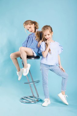 Kızlar ikizler mavi elbise bir barın yakınında poz ışık mavi bir arka plan üzerinde tabure.