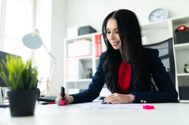 Güzel genç kız masa ofis belgeleri ile çalışıyor. Kız belgedeki önemli noktaları pembe bir marker ile vurgulamaktadır..