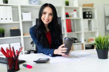 Güzel bir genç kız bir bardak kahve tablo ofiste bir sandalyede oturup ile düzenliyor.