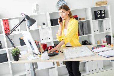 Genç bir kız bir masanın ayakta, telefonda konuşurken ve bir bilgisayarla çalışma. Önce kız masanın üzerinde bir manyetik tahta