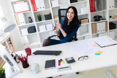 Genç bir kız ofiste masada oturur ve onun elinde kalem tutan.