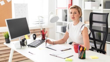 Genç sarışın kız ofiste bilgisayar masasında oturur ve onun elinde kalem tutan.