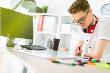 Gözlüklü genç bir adam bir bilgisayar masası duruyor. Genç bir adam bir işaretleyici manyetik bir tahtaya çizer. Çocuklar kulaklık boynuna asmak.