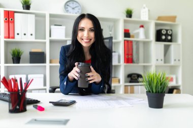 Güzel bir genç kız bir bardak kahve tablo ofiste bir sandalyede oturup ile düzenliyor.