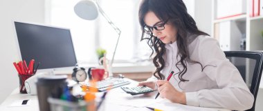 Genç bir kız bir hesap makinesi ve belgeleri çalışma office masada oturuyor.