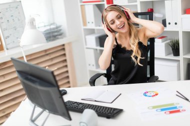 Genç bir kız ofiste bilgisayar masasında oturur ve kulaklık aracılığıyla müzik dinler.