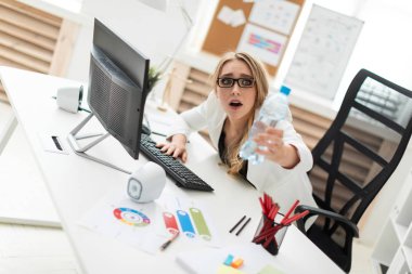 Korkmuş bir genç kız ofiste bir masada oturur ve bir şişe su tutar.