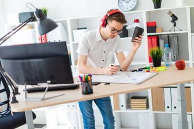 Gözlük ve kulaklık genç bir adamla bir bardak kahve elinde tutuyor ve bir işaretleyici tahtaya çizer.