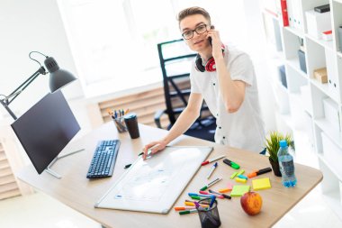 Gözlüklü genç bir adam bir bilgisayar masası duruyor ve telefonda konuşuyor. Önce onu bir manyetik kurulu ve işaretleri yatıyor. Çocuklar kulaklık boynuna asmak.