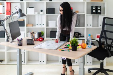 Genç bir kız bir bilgisayar masası duruyor ve bir işaretleyici manyetik bir tahtaya çizer.