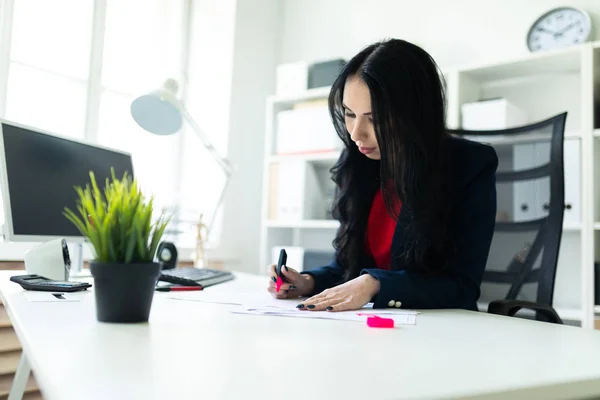 Schöne junge Mädchen arbeitet mit Dokumenten im Büro am Tisch. das Mädchen unterstreicht wichtige Punkte im Dokument mit einem rosafarbenen Marker. — Stockfoto