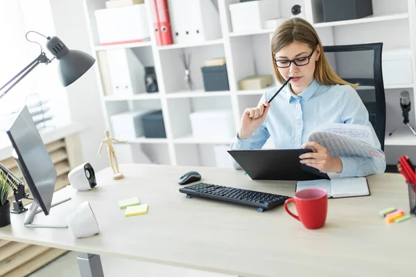 En ung pige med briller sidder ved et bord på kontoret, holder en blyant i hånden og arbejder med dokumenter. . - Stock-foto