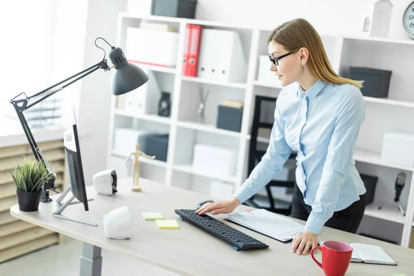 Молодая девушка в очках стоит рядом со столом и печатает на клавиатуре. — стоковое фото