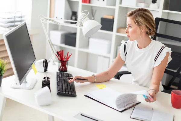 Een jong blond meisje zit achter een computerbureau in het kantoor, houdt een potlood in haar hand en werken met documenten. — Stockfoto