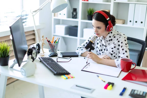 Menina bonita está sentada em fones de ouvido e com um microfone na mesa no escritório . — Fotografia de Stock