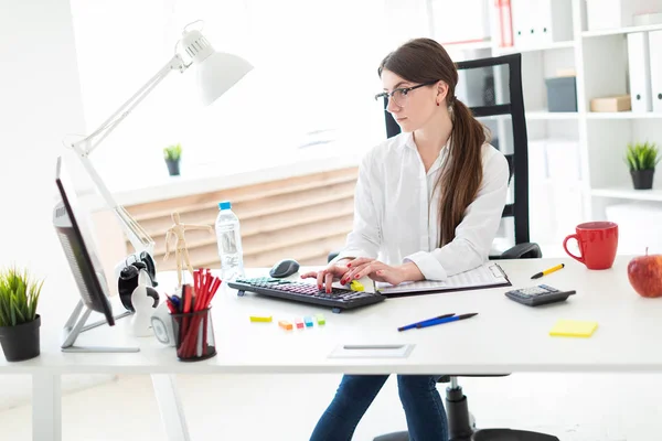 En ung flicka sitter vid ett bord på kontoret och skriva på tangentbordet. — Stockfoto