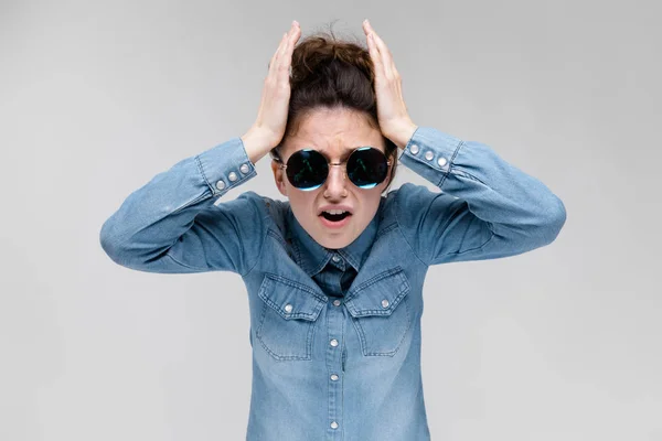 Jonge brunette meisje in ronde bril. Haren worden verzameld in een broodje. Het meisje houdt haar handen achter haar hoofd. — Stockfoto