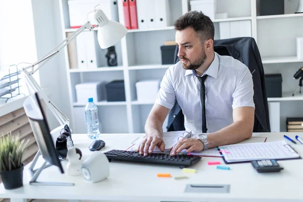 Ein Mann sitzt an einem Tisch im Büro und arbeitet mit Dokumenten und einem Computer. — Stockfoto