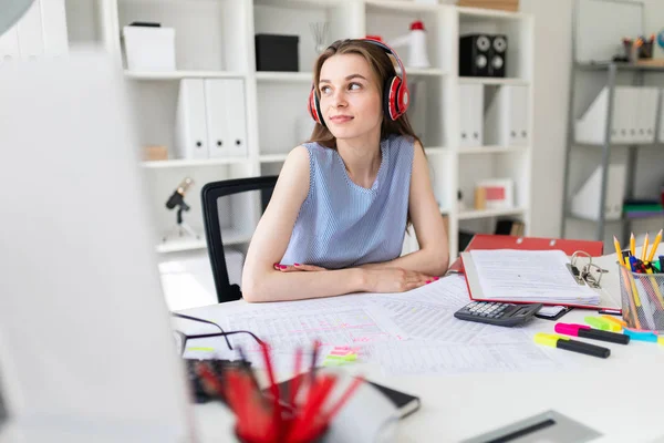 Menina bonita no escritório senta-se a uma mesa em fones de ouvido vermelhos . — Fotografia de Stock