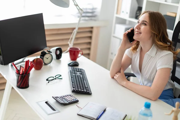 Mooi jong meisje is in het bureau zitten en praten over de telefoon. — Stockfoto