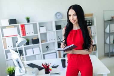 Kırmızı elbiseli güzel genç kız ofiste duran ve bir defter ve bir kalem tutan.