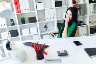 Genç bir kız ofiste masada oturur ve onu gözlük kafasına yükseltir.