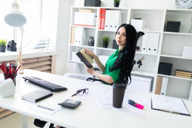 Genç bir kız ofis masa başında oturan ve bir kitap tutuyor.