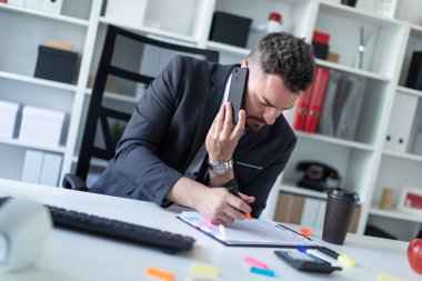 Bir adam ofiste masa başında oturan, telefonda konuşurken ve bir işaretleyici belgeye yazma.