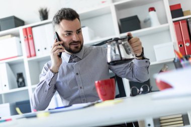 Ofiste genç bir adam telefonda konuşurken ve bir cezve tutan bir masada oturur.