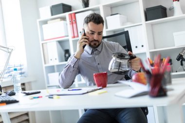 Ofiste genç adam masada oturan, telefonda konuşurken ve cezve seyir.