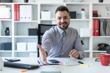 Genç bir adam ofiste bir masada oturur ve elini tutar. Adamın biri tebrik.