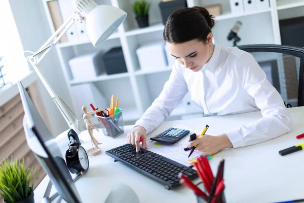 Uma jovem no escritório senta-se a uma mesa, trabalha com um computador, calculadora, documentos e segura um marcador e uma caneta na mão esquerda. . — Fotografia de Stock